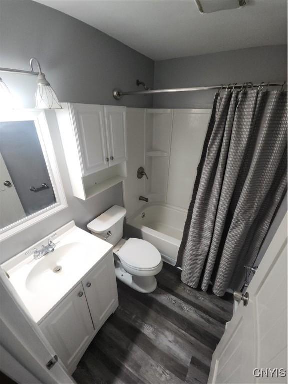 full bathroom featuring hardwood / wood-style flooring, shower / tub combo with curtain, vanity, and toilet