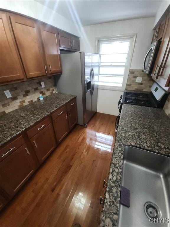 kitchen featuring appliances with stainless steel finishes, dark hardwood / wood-style floors, dark stone countertops, and backsplash