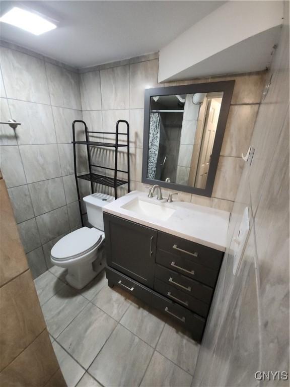 bathroom with a shower with curtain, vanity, toilet, and tile walls