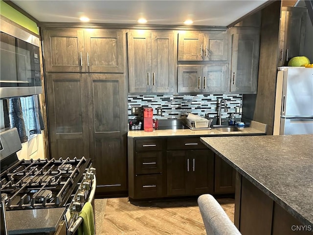 kitchen with sink, dark brown cabinets, light wood-type flooring, stainless steel appliances, and backsplash