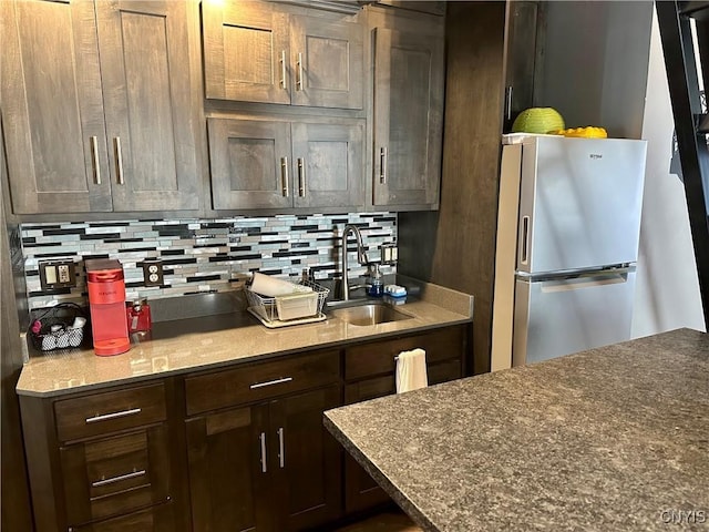 kitchen featuring sink, dark brown cabinets, stainless steel refrigerator, stone counters, and decorative backsplash