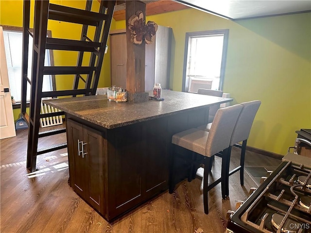 kitchen with dark stone counters, a center island, dark brown cabinetry, dark wood-type flooring, and stainless steel range with gas stovetop