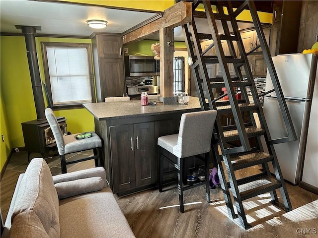 bar with stainless steel appliances, dark brown cabinets, a wood stove, and dark hardwood / wood-style floors