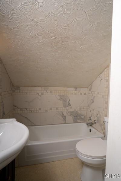 bathroom featuring lofted ceiling, toilet, a textured ceiling, and a washtub