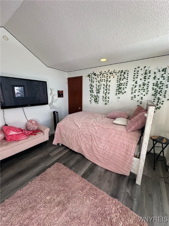 bedroom with dark wood-type flooring, lofted ceiling, and a textured ceiling