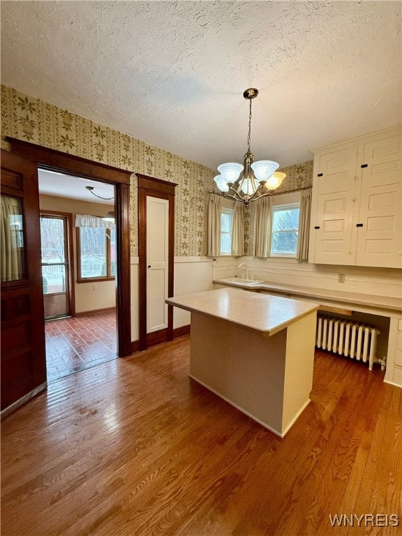 kitchen featuring wood-type flooring, a center island, a textured ceiling, radiator heating unit, and pendant lighting