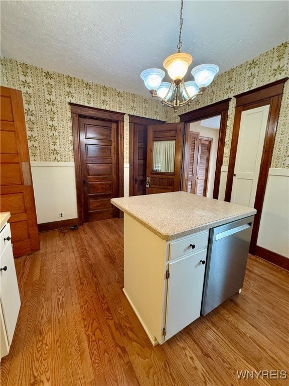 kitchen featuring white cabinetry, hanging light fixtures, stainless steel dishwasher, a textured ceiling, and light hardwood / wood-style flooring