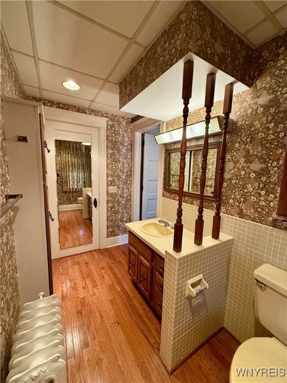 bathroom with tile walls, hardwood / wood-style flooring, vanity, toilet, and a drop ceiling