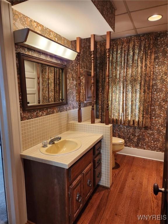 bathroom with a paneled ceiling, backsplash, hardwood / wood-style flooring, vanity, and toilet