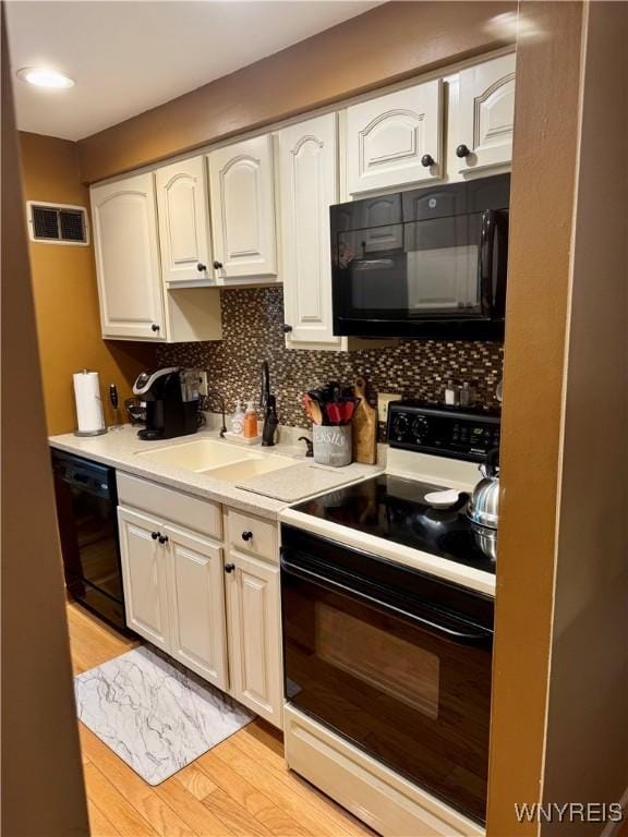 kitchen with tasteful backsplash, sink, white cabinets, black appliances, and light wood-type flooring