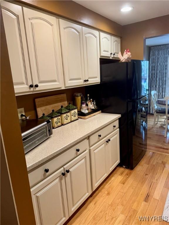 kitchen with white cabinetry, light stone countertops, black refrigerator, and light hardwood / wood-style floors