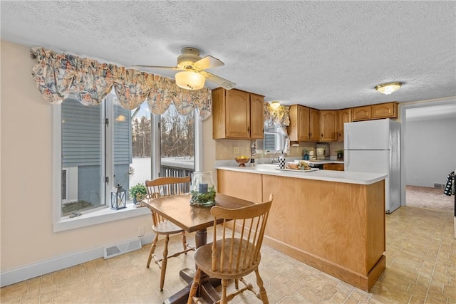 kitchen with white fridge, a textured ceiling, ceiling fan, and kitchen peninsula