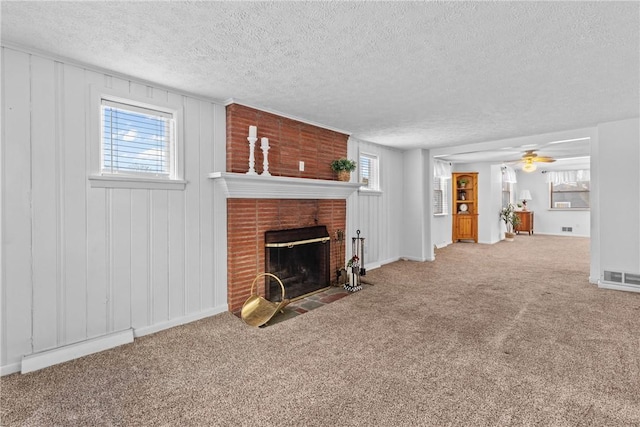 unfurnished living room featuring a textured ceiling, a brick fireplace, ceiling fan, carpet, and a baseboard heating unit