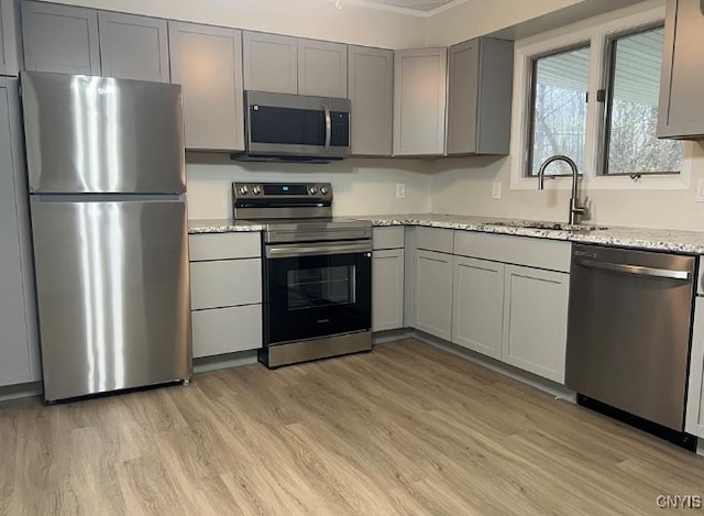 kitchen with sink, gray cabinetry, stainless steel appliances, light stone countertops, and light wood-type flooring