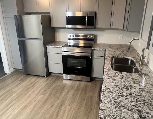 kitchen featuring appliances with stainless steel finishes, sink, light stone counters, and light wood-type flooring