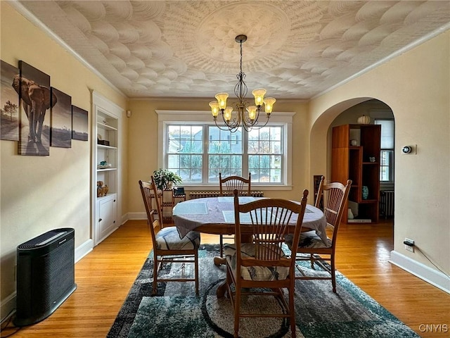 dining space with an inviting chandelier, crown molding, built in features, and light hardwood / wood-style floors