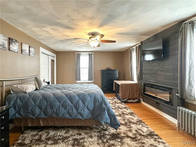 bedroom with hardwood / wood-style flooring, radiator heating unit, ceiling fan, and a closet