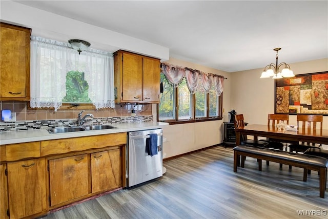 kitchen featuring pendant lighting, sink, decorative backsplash, stainless steel dishwasher, and light hardwood / wood-style flooring