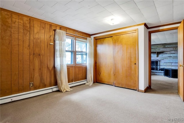 unfurnished bedroom featuring wooden walls, a baseboard heating unit, crown molding, light carpet, and a closet