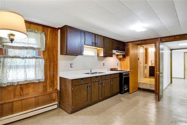 kitchen with stainless steel range with gas cooktop, wooden walls, a baseboard radiator, sink, and dark brown cabinetry