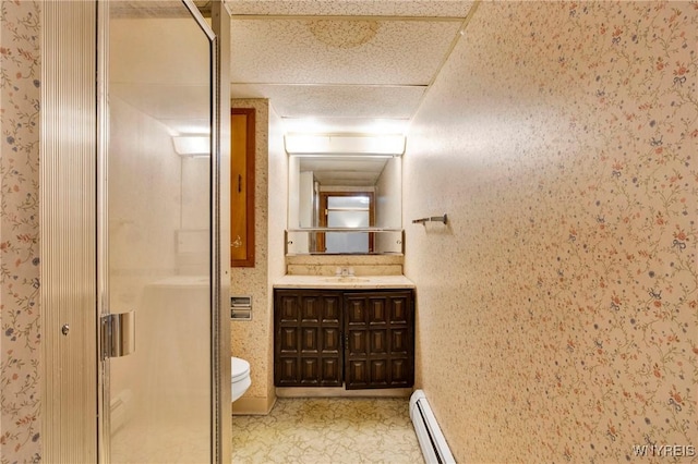 bathroom with toilet, a shower with shower door, vanity, a baseboard heating unit, and a drop ceiling