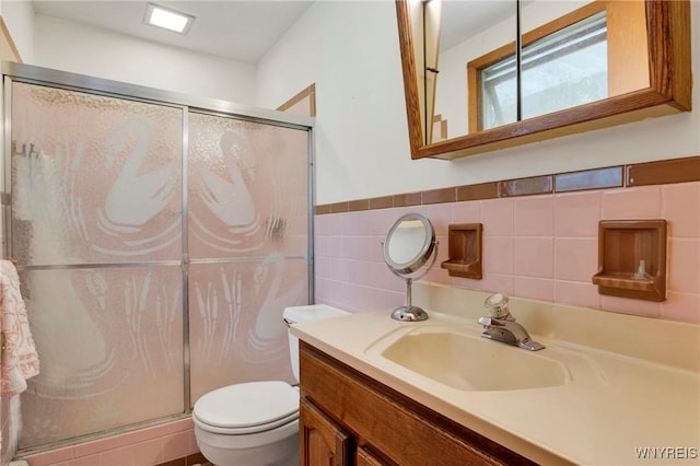 bathroom featuring vanity, toilet, a shower with shower door, and tile walls