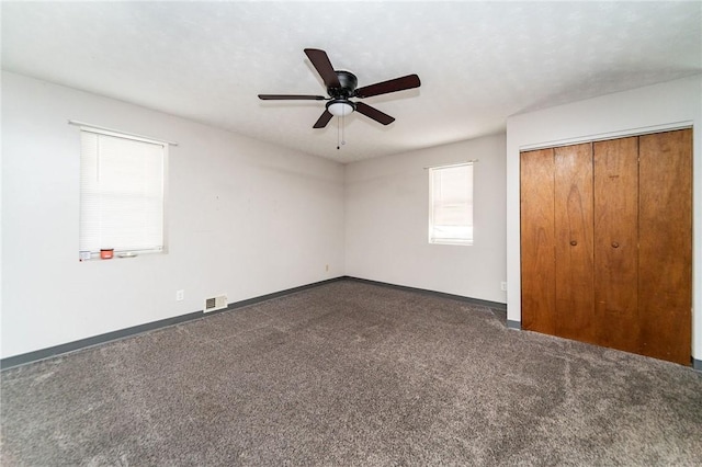 unfurnished bedroom featuring ceiling fan, dark carpet, and a closet