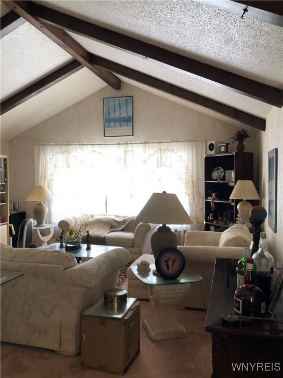 carpeted living room with lofted ceiling with beams and a textured ceiling