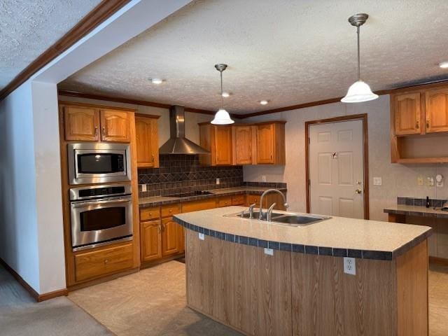 kitchen with wall chimney exhaust hood, sink, a center island with sink, pendant lighting, and stainless steel appliances