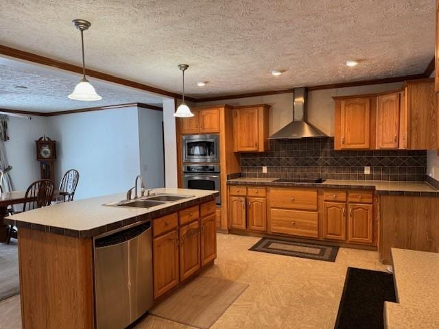 kitchen featuring appliances with stainless steel finishes, pendant lighting, sink, wall chimney range hood, and a center island with sink