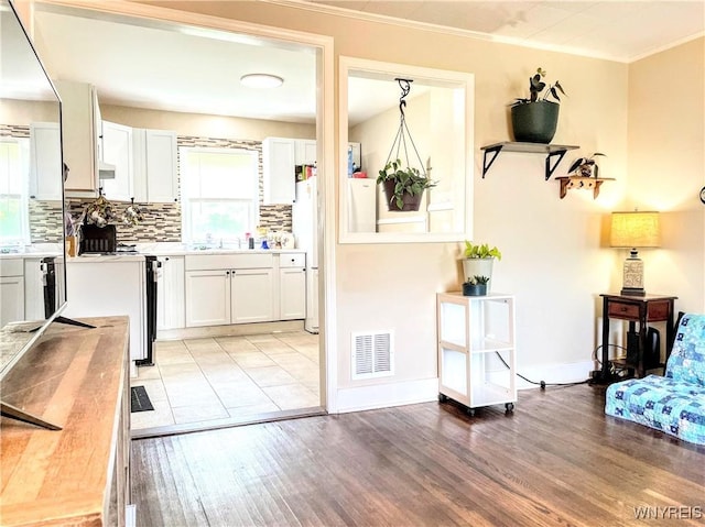 kitchen featuring white cabinetry, ornamental molding, light hardwood / wood-style flooring, and decorative backsplash