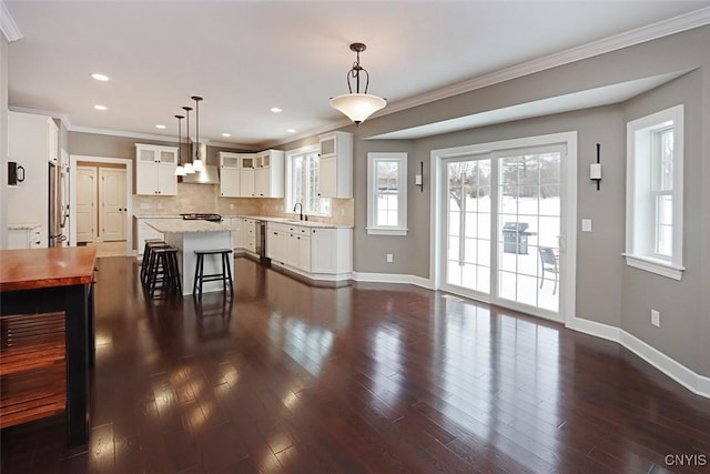 kitchen with a center island, a kitchen breakfast bar, pendant lighting, wall chimney range hood, and white cabinets