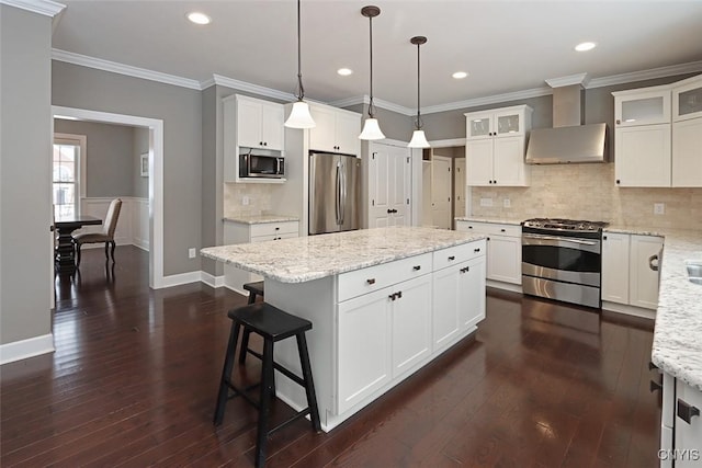 kitchen featuring white cabinetry, appliances with stainless steel finishes, hanging light fixtures, and wall chimney range hood