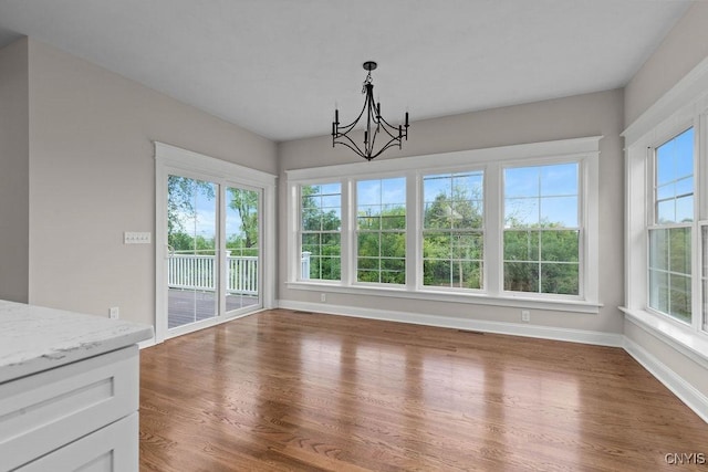 unfurnished dining area with plenty of natural light, a notable chandelier, and dark hardwood / wood-style flooring