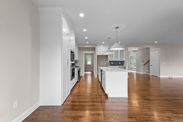 kitchen with pendant lighting, a kitchen island with sink, white cabinetry, stainless steel appliances, and dark hardwood / wood-style flooring