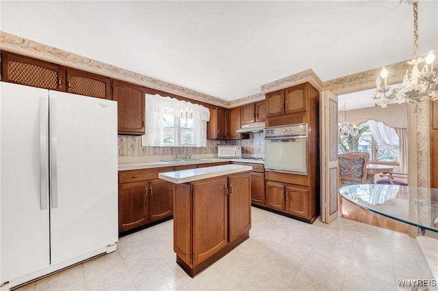 kitchen with sink, a center island, a chandelier, pendant lighting, and white appliances