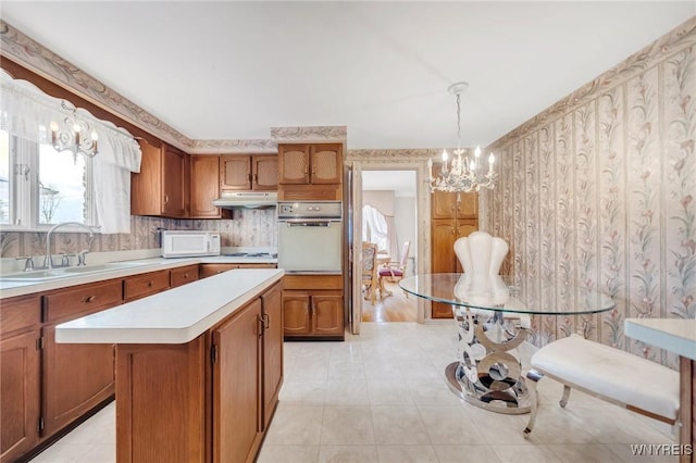 kitchen with sink, decorative light fixtures, a chandelier, a center island, and white appliances