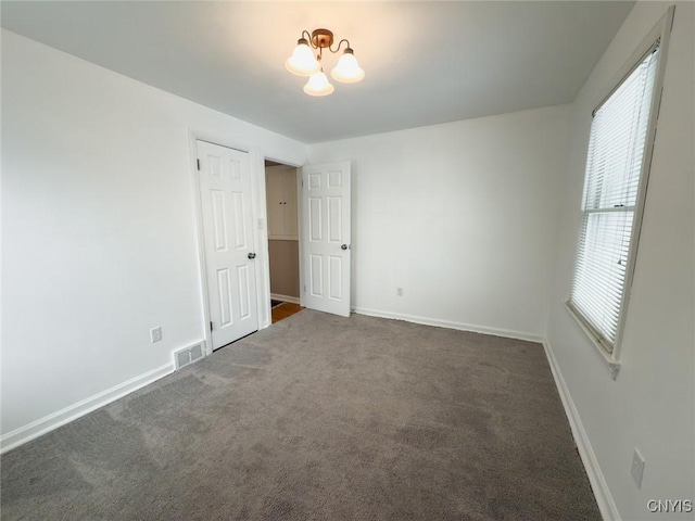 unfurnished bedroom with an inviting chandelier and dark colored carpet