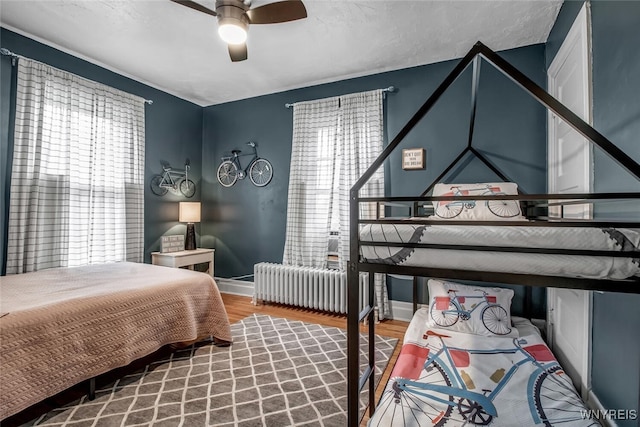 bedroom with ceiling fan, radiator heating unit, hardwood / wood-style floors, and multiple windows