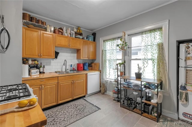 kitchen featuring sink, crown molding, light tile patterned floors, white dishwasher, and decorative backsplash