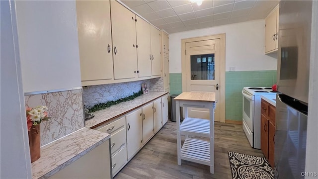 kitchen featuring light hardwood / wood-style flooring, stainless steel fridge, white range with electric cooktop, tile walls, and white cabinets