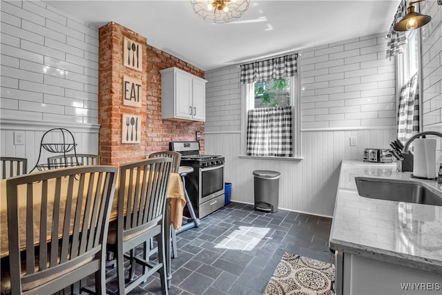 kitchen featuring brick wall, stainless steel range with gas cooktop, sink, white cabinets, and light stone counters