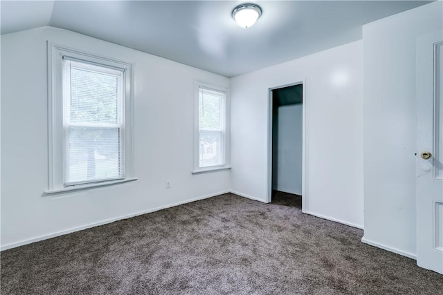 unfurnished bedroom with lofted ceiling, dark carpet, and multiple windows