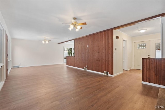 unfurnished living room featuring wood walls, ceiling fan, visible vents, and wood finished floors