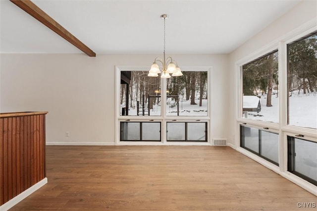 unfurnished dining area with baseboards, visible vents, wood finished floors, beam ceiling, and a notable chandelier