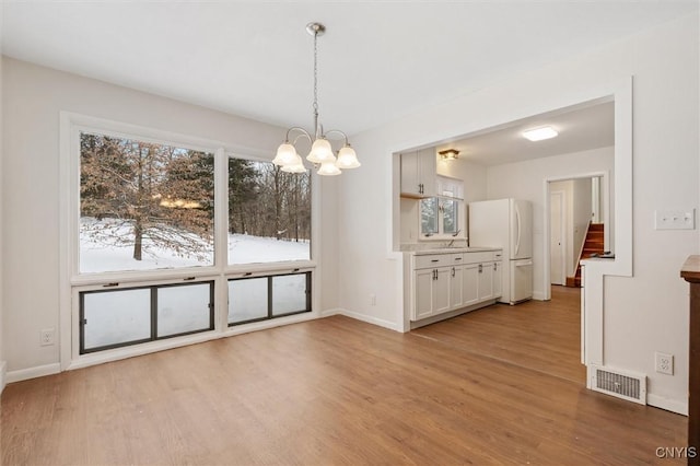 unfurnished dining area with stairway, visible vents, light wood-style flooring, and baseboards