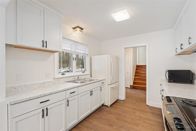 kitchen featuring electric range, a sink, freestanding refrigerator, and white cabinetry