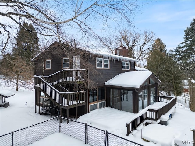 snow covered back of property with a chimney, a sunroom, fence private yard, a wooden deck, and stairs