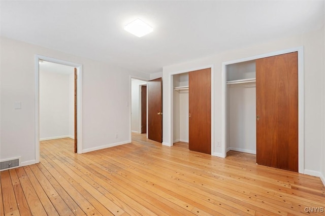 unfurnished bedroom with baseboards, light wood-style flooring, visible vents, and two closets