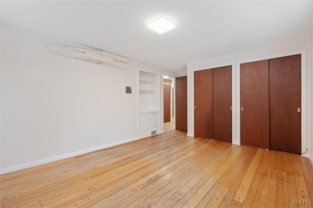 unfurnished bedroom with multiple closets, visible vents, light wood-style flooring, and baseboards